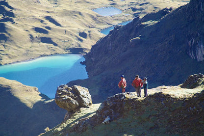 Three people standing on a rocky outcrop overlooking a scenic landscape with lakes and mountains.