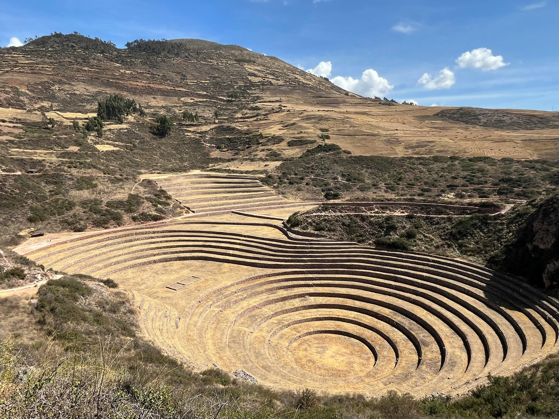 Terraced agricultural patterns on a hillside under a blue sky with clouds.