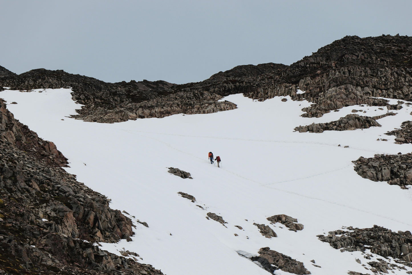 Two people hiking on a snowy mountain landscape with rocky terrain.