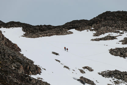 Two people hiking on a snowy mountain landscape with rocky terrain.