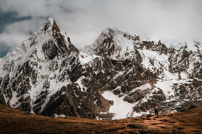 Snow-capped mountain range with a person standing at the base on a cloudy day.